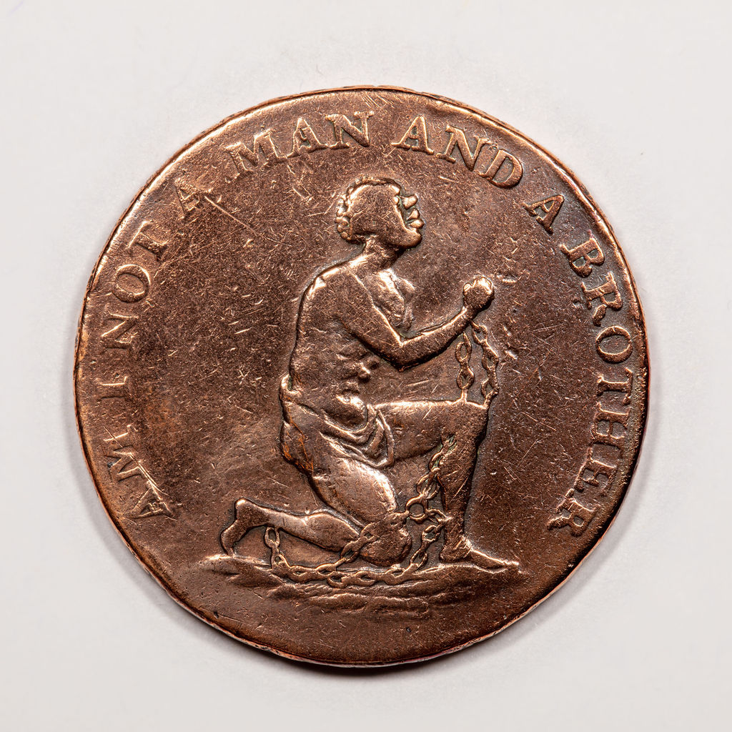 Circular coin-like token showing a man on one knee with his hands shackled. Around the edge are the words 'Am I not a man and a brother'