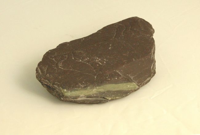 A dark coloured rock made up of horizontal layers which can be seen on the edge of the sample