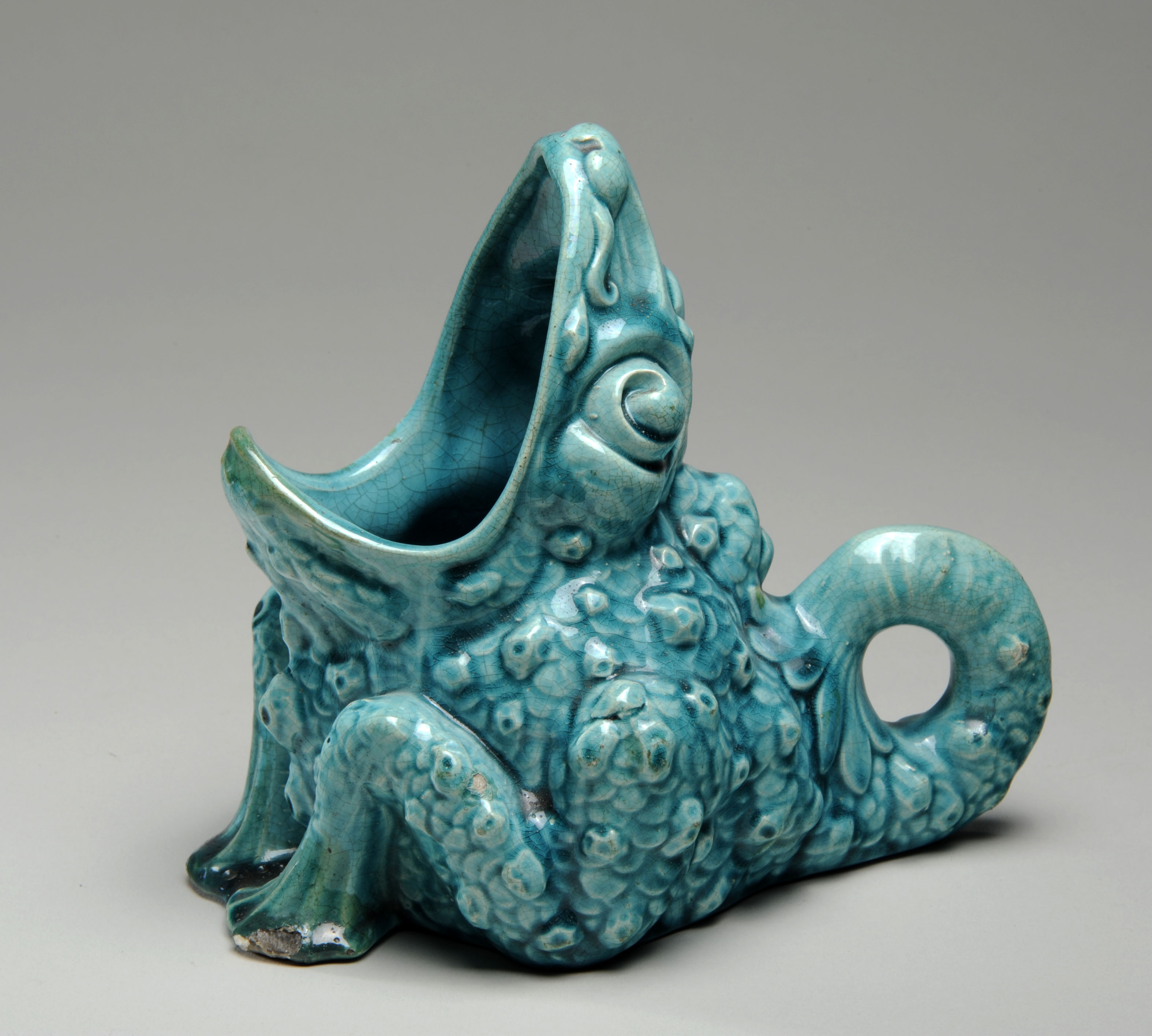 Turquoise ceramic frog sitting down with its mouth turned upwards. Its mouth is wide open