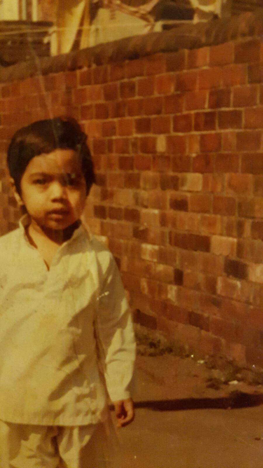 Old colour photograph of a young boy wearing a white long sleeved shirt and white trousers.