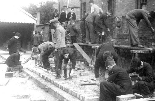 First of two photographs showing schoolboys building an air raid shelter using bricks.