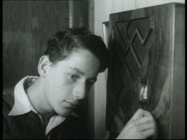 Boy tuning in family radio, circa 1950.  He is leaning his head towards the radio while turning a dial.
