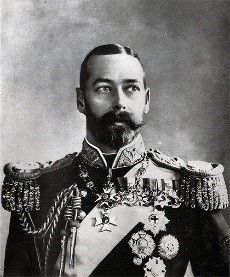 Black and white portrait of King George V.  He wears a big moustache and a beard, his jacket has a high collar and tasselled epaulettes and has several medals pinned to it.