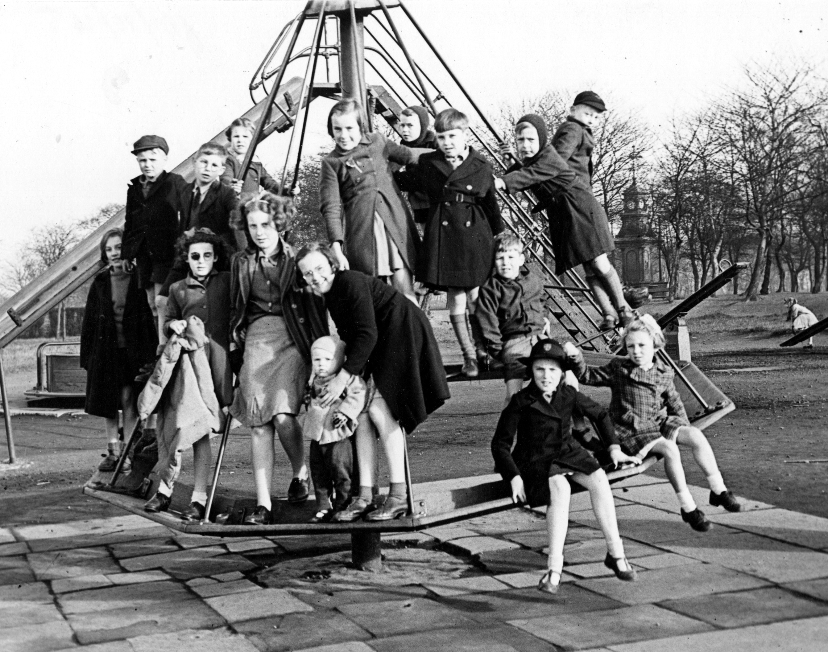 Children crowding onto a roundabout in Woodhouse Moor playground.  Paving slabs are underneath the roundabout.