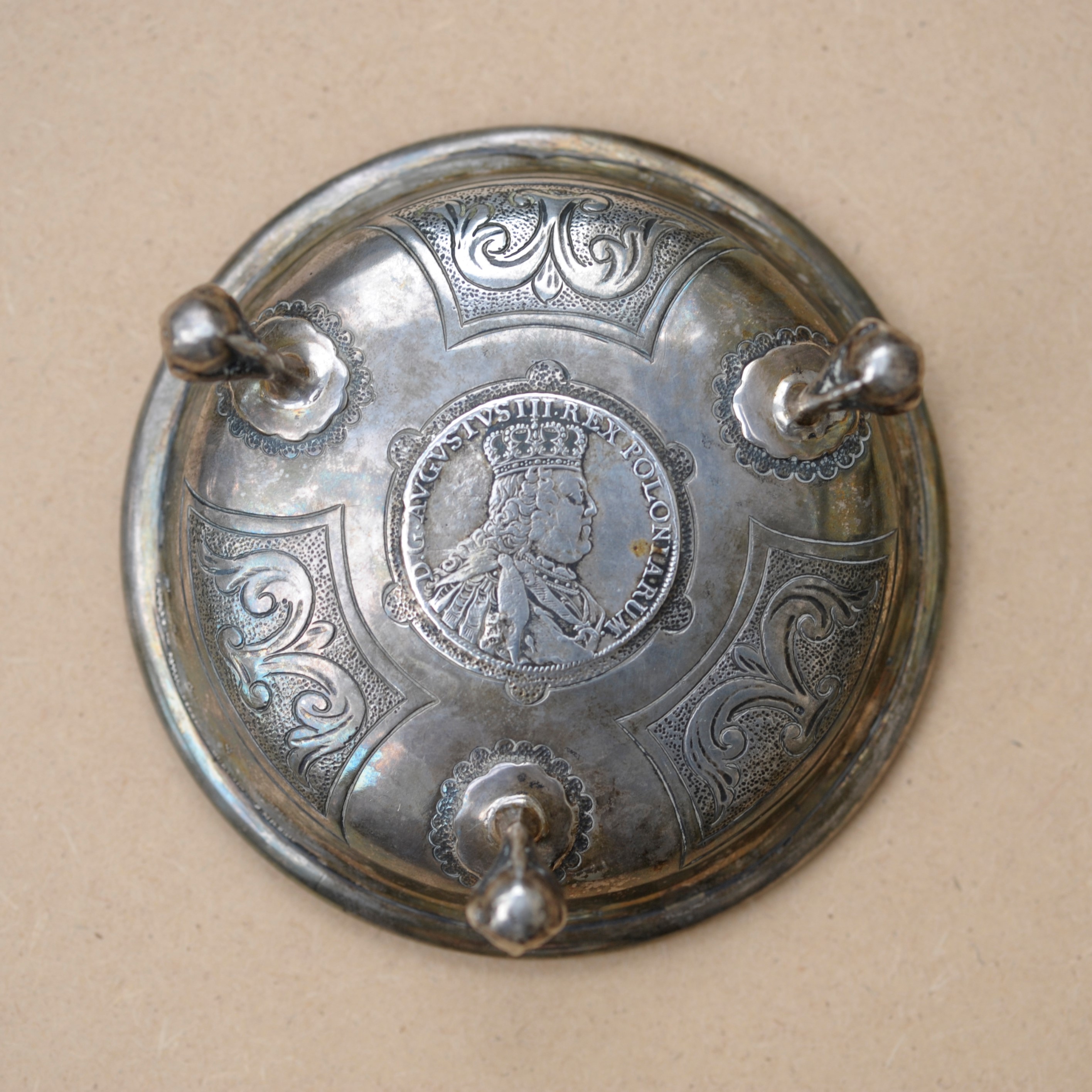 Silver stand with the coin at the centre of the stand. The heads side of the coin can be seen.