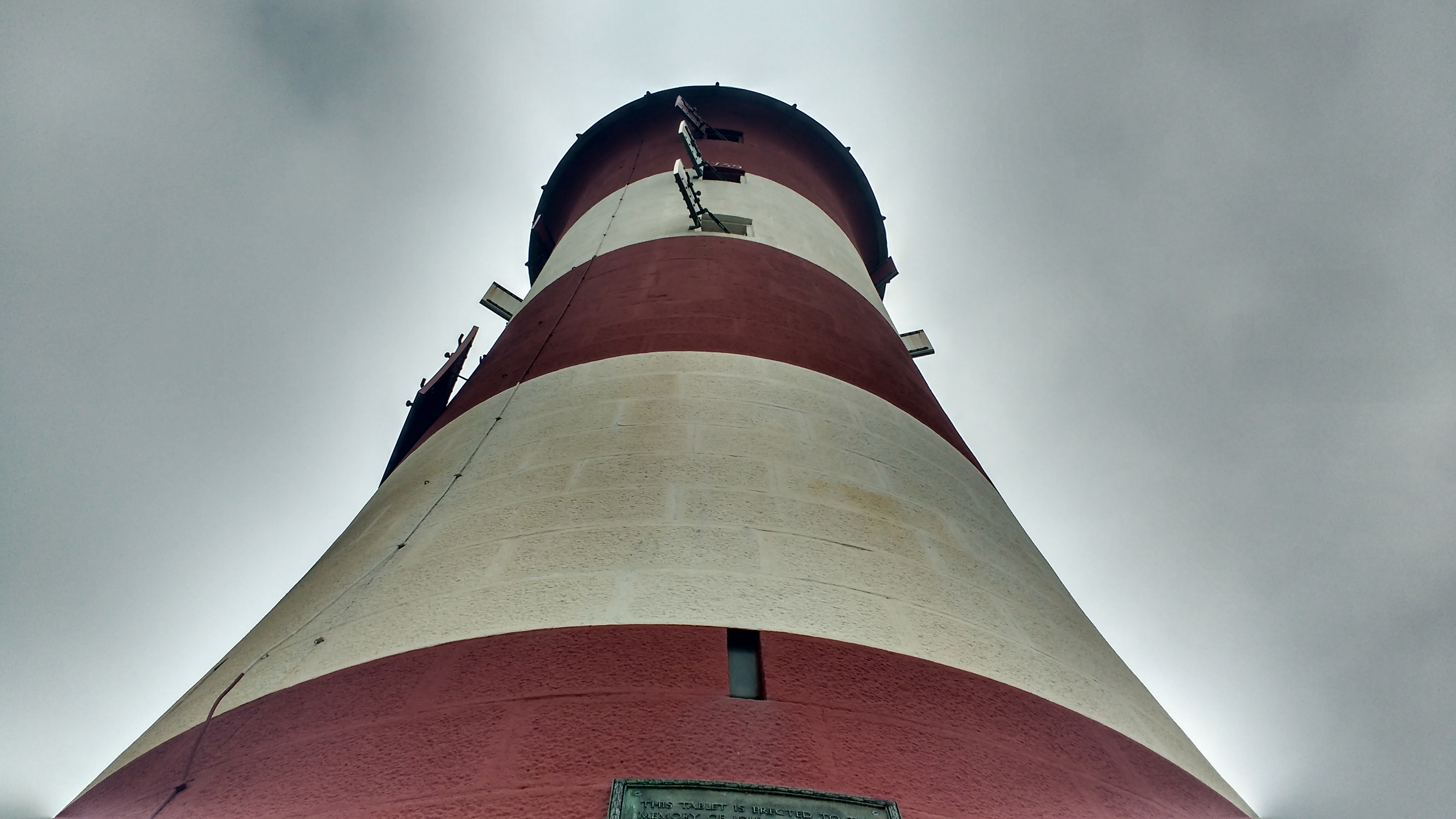 A photo of the top of a red and white stripped tower, extreme perspective facing up the tower shaft.