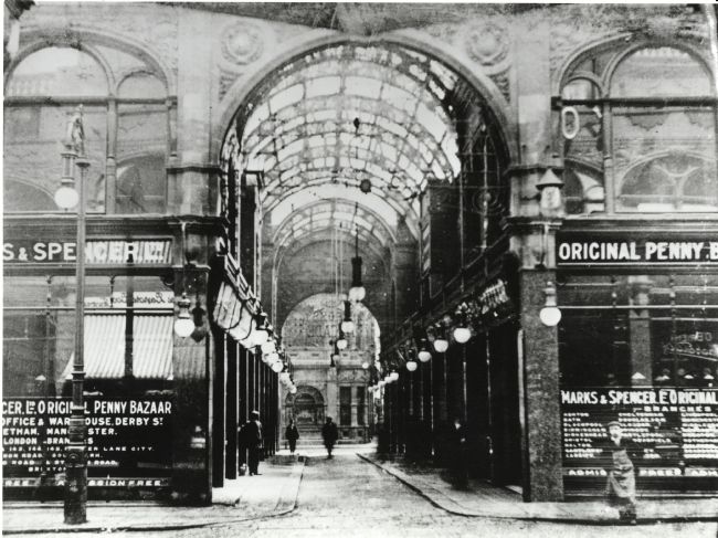 Black and white photo of early 20th Century shopping arcade with Marks  & Spender Penny Bazaar signage over shop frontages
