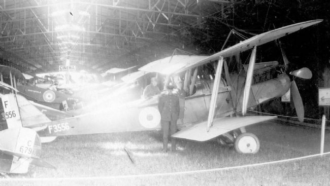 Black and white photograph of First World War aircraft with two men seated in the cockpit and one man standing by the plane