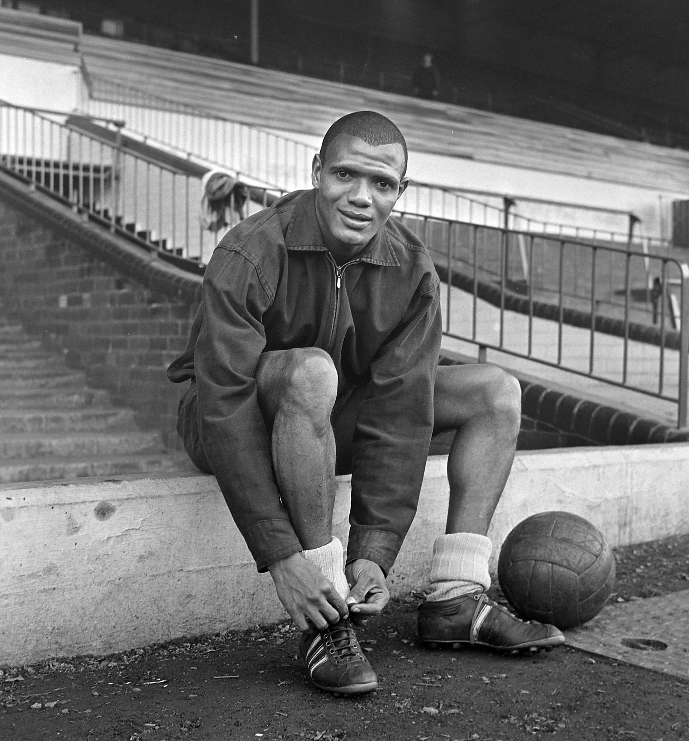 Black and white photograph of Albert sitting on some steps tying up his football boots