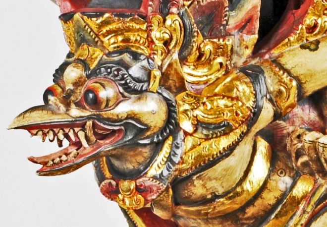 Close-up of the face, showing bulging eyes, beak open with lots of teeth and tongue.  The statue is gold leafed and painted red and black.