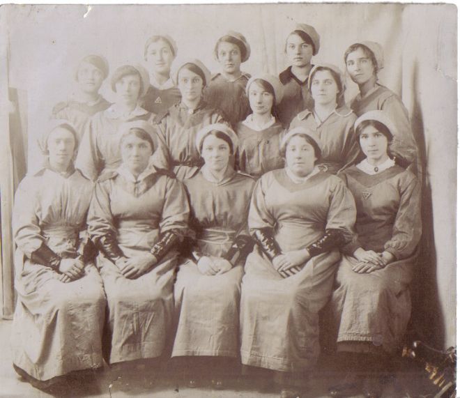 Group photograph of female factory workers.  they are wearing leather (?) gauntlets for protection.