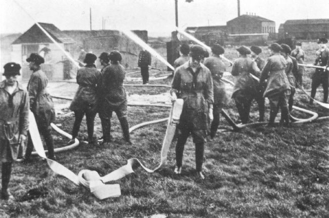 Photograph showing women taking part in a fire practice at the Barnbow Munitions Factory in Leeds.  They are holding hoses with water jetting out.