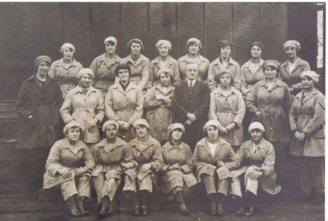 Black and white photograph showing female factory workers.  There is a male in the centre, probably the factory manager.