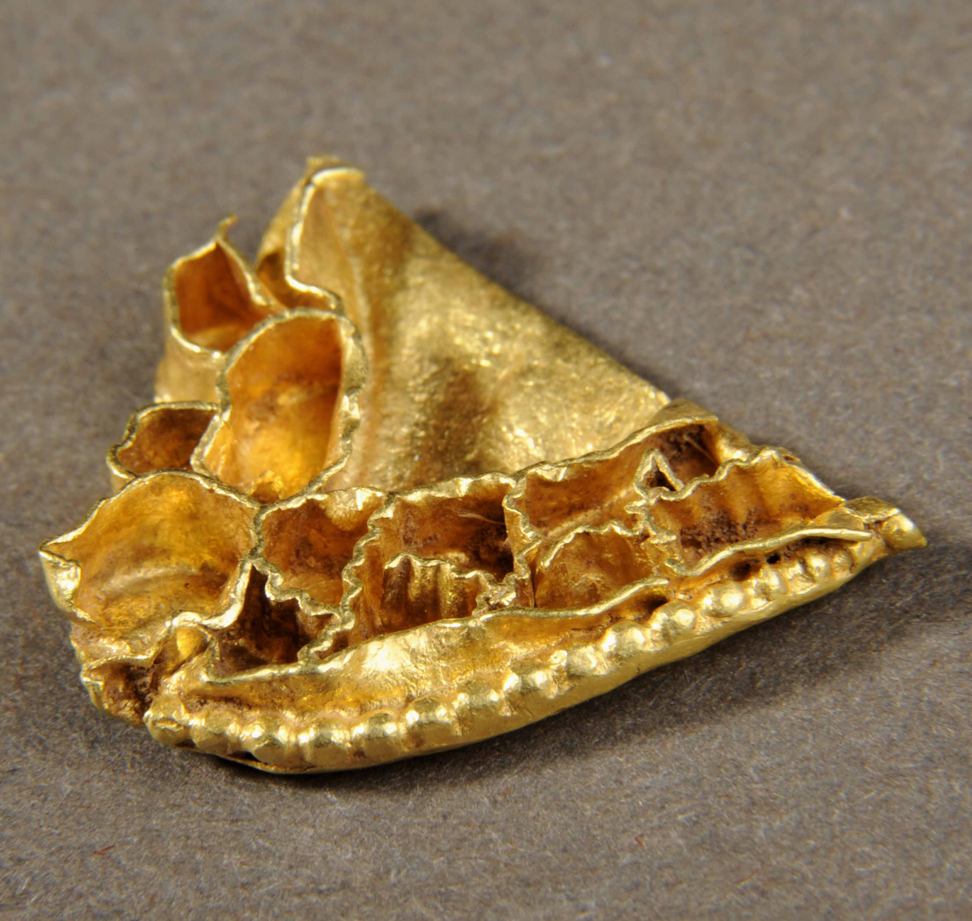 Triangular shaped fragment of gold, showing small cells for the inlay of gems.  The fragment is squashed and mis-shapen.