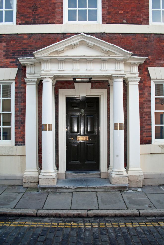 Close up photo of the front of a grand red brick house.  The doorway is flanked by white painted pillars.
