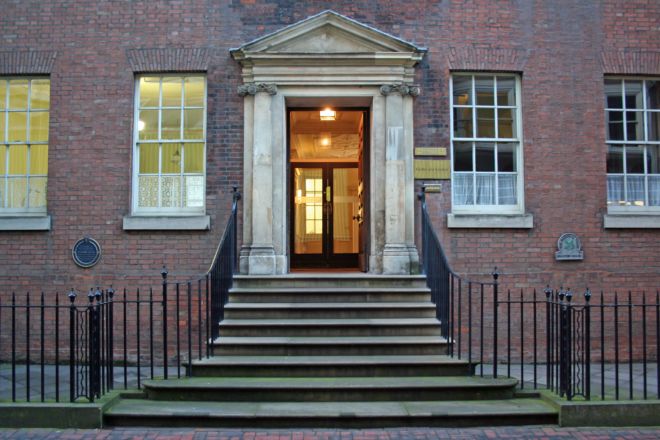 Entranceway of a house showing steps up to a grand front door.  Either side are large sash windows.