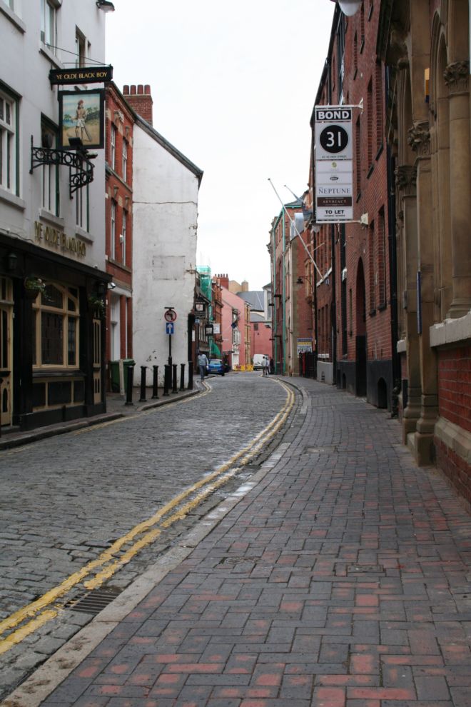 View down Hull high street showing a narrow cobbled road lined with buildings on each side.