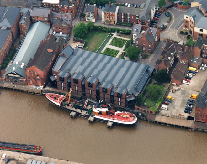 Photograph shows the water, with a boat moored next to old warehouses.
