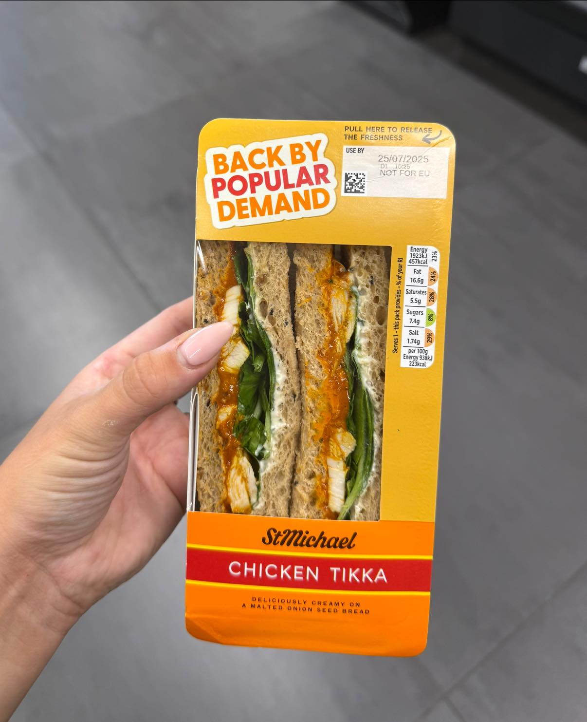Hand holding a St Michael Chicken Tikka sandwich in bright yellow packaging.