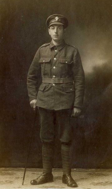Black and white photo showing Hyman in WW1 uniform.  He wears a peaked cap and is standing up straight  with a cane in his right hand.