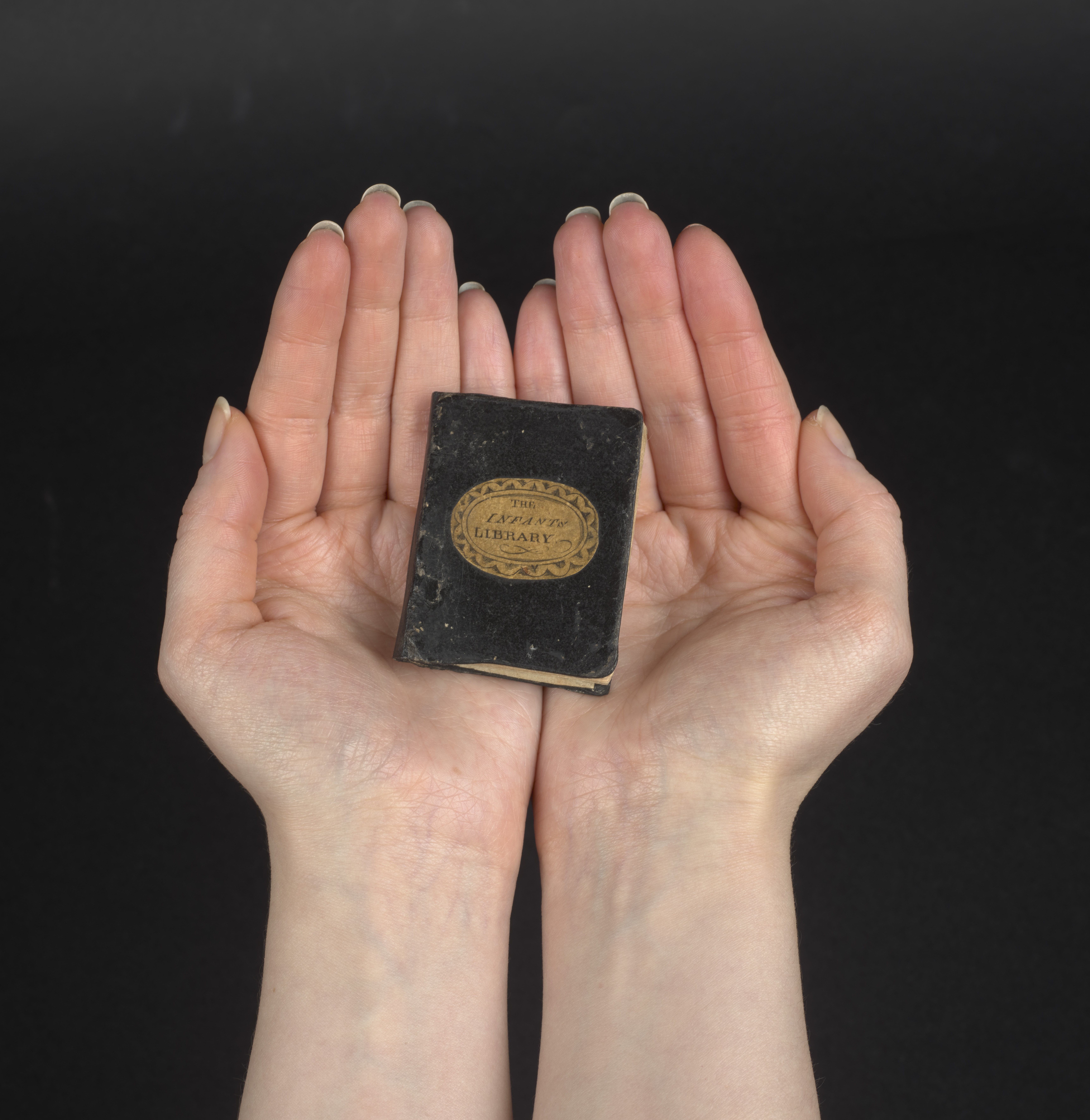 An adult’s hand with a mini book in the palm. The book only covers about half of the palm.