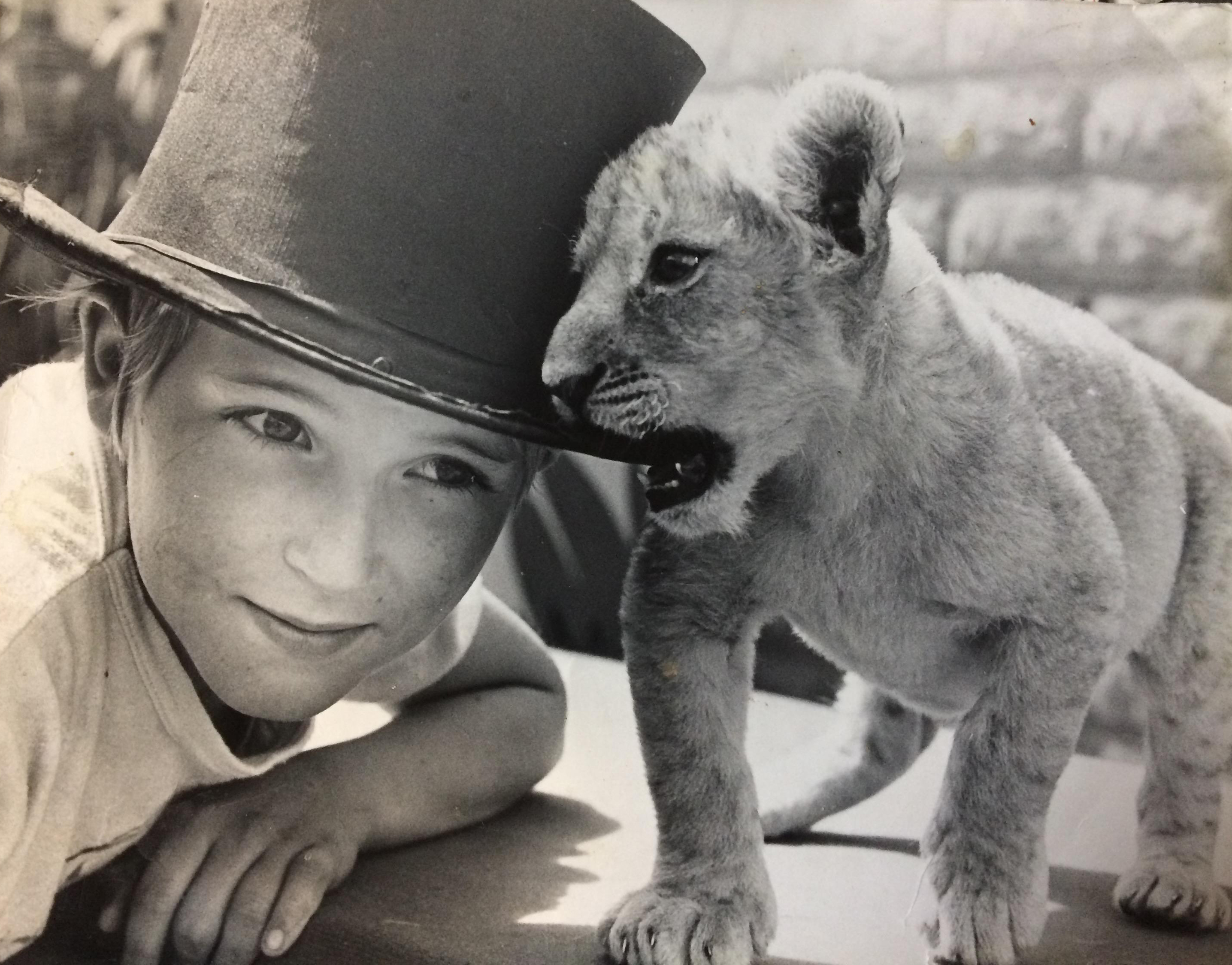 Carl Denver as a young boy wearing a top hat.  A young lioness cub has the brim of the hat in her mouth.