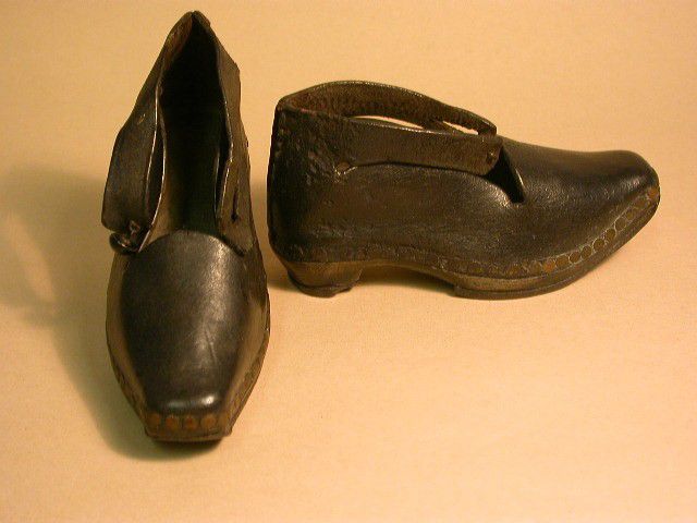 Small pair of dark brown leather clogs with wooden soles.  The leather uppers are attached to the sole using metal tacks.