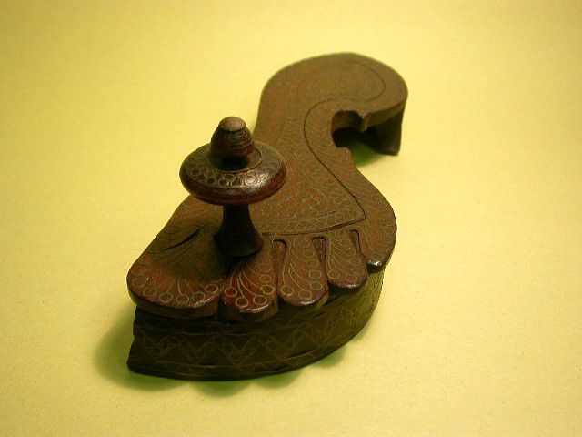 Wooden sandal made in the shape of a footprint. From the area between the big toe and the next toe there is a wooden peg shaped like a mushroom sticking up.