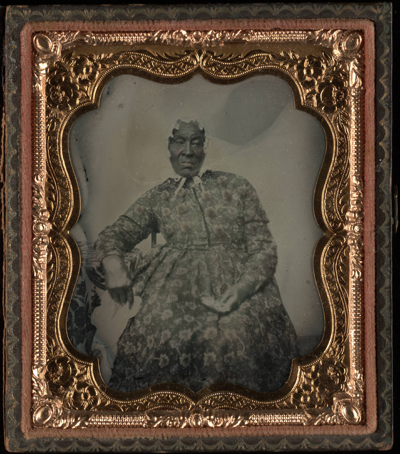 Three quarter length portrait, seated elderly black woman with fancy dress and white bonnet, holding handkerchief and glasses