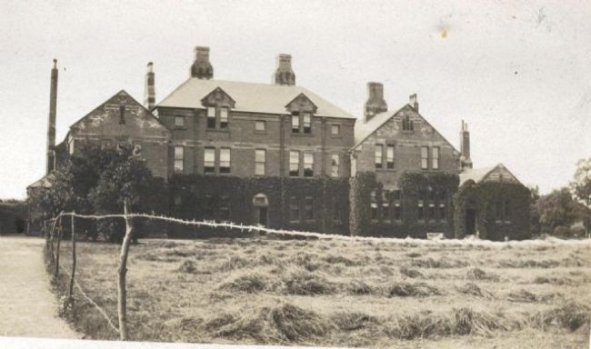 Black and white photo of hay being grown outside a barrack building in Riding