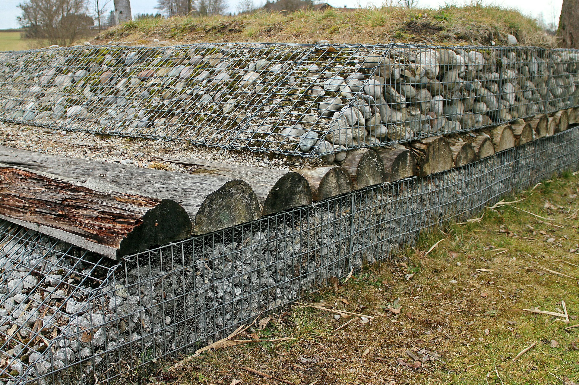 Colour photograph showing a layer of rocks, a layer of tree trunks cut in half longways and another layer of rocks