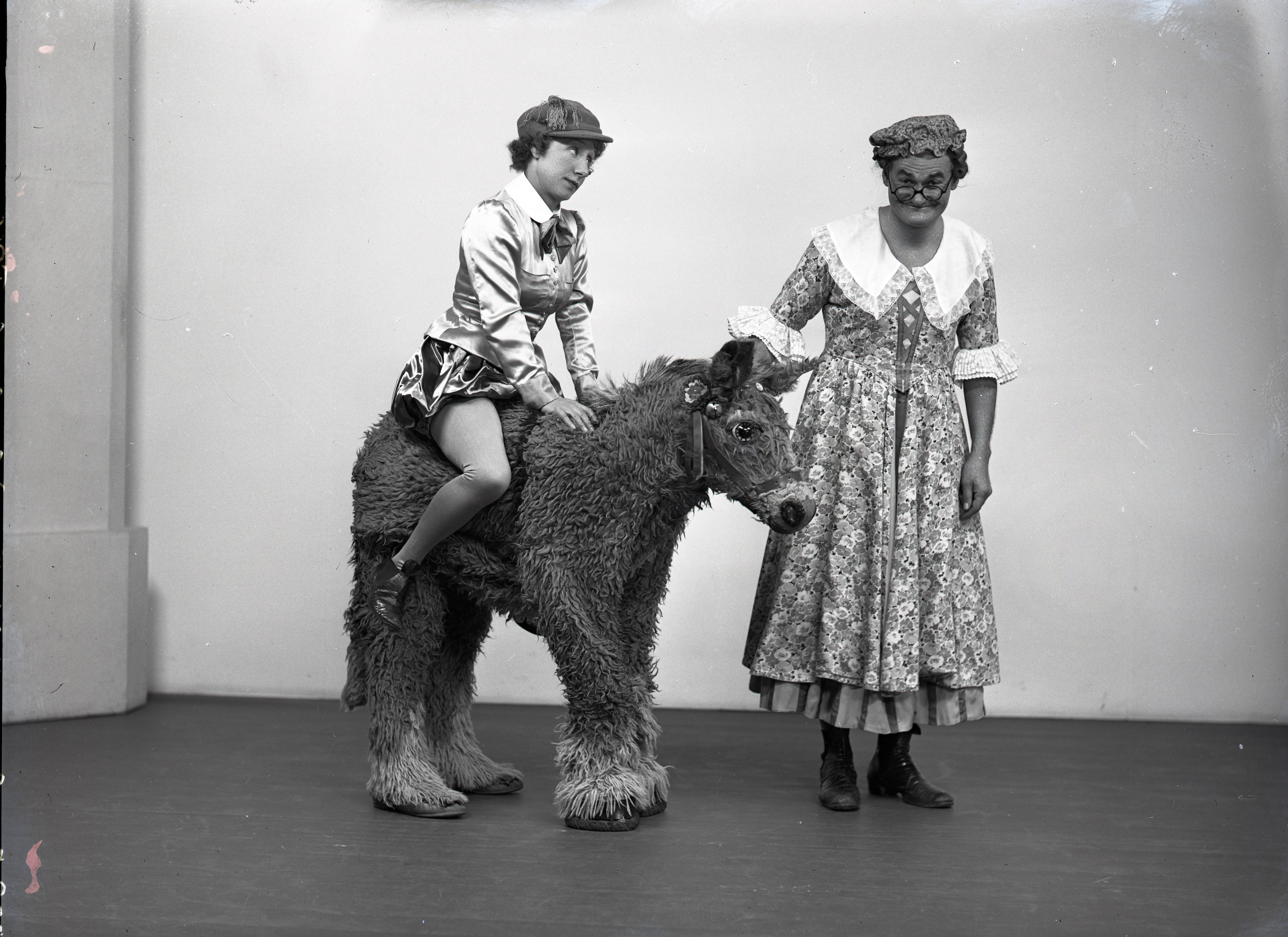 Black and white photo showing two actors, one of whom is sitting on a model pony