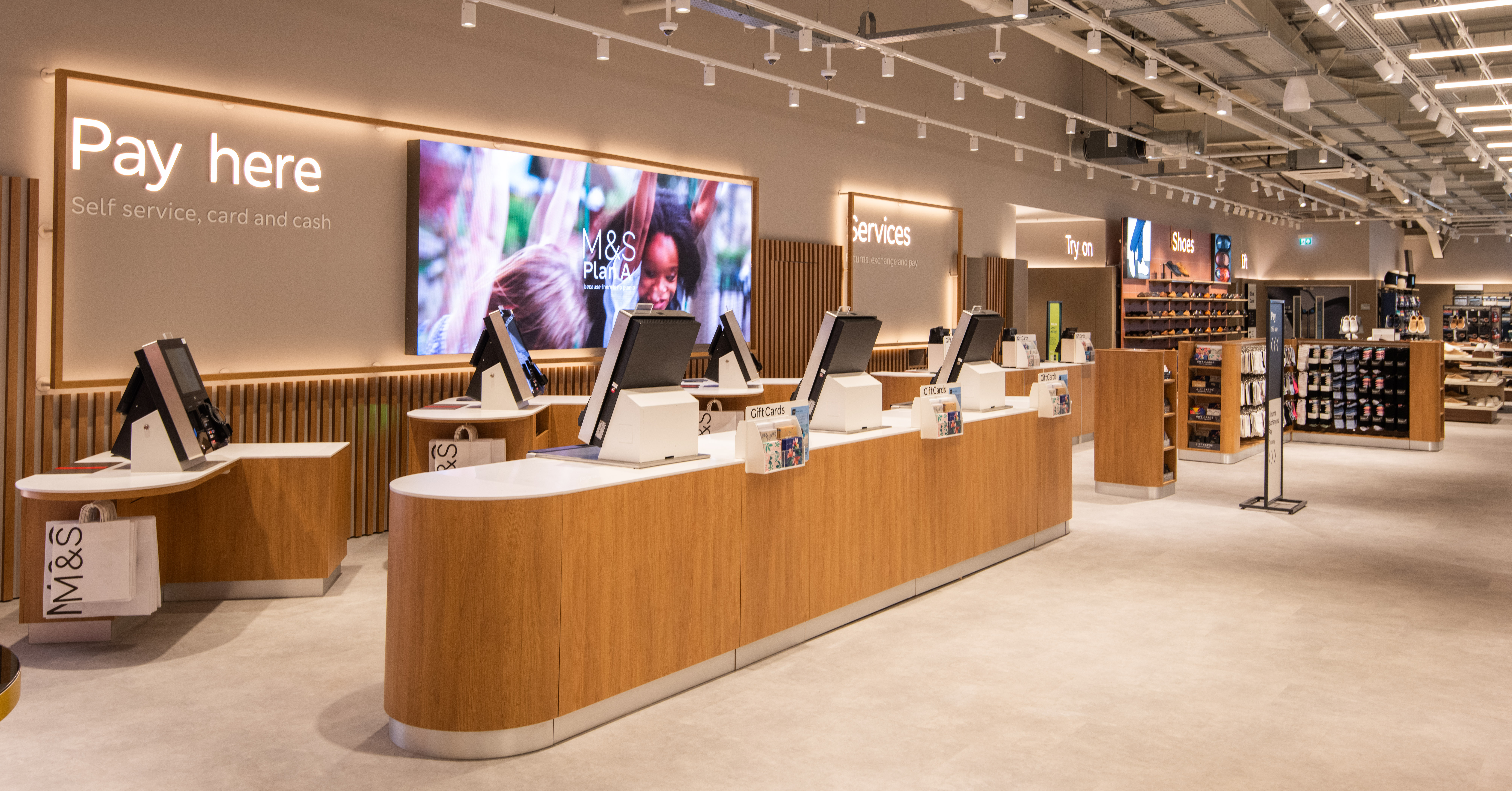 Modern self-checkout area in a Marks & Spencer store with wooden counters, digital screens, and signs for payment and services. Bright, organized, and welcoming.
