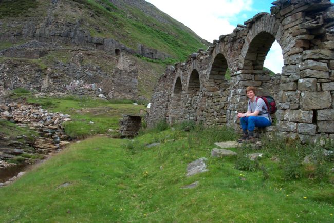 Two ruined stone buildings.  One is the old peat store, with a series of arches.  In the distance is a huge pile of stones that used to be the mill