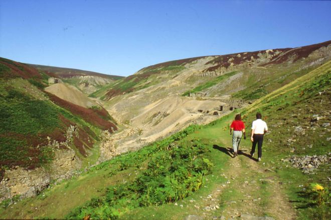 Walkers enjoying a stroll up a moorland valley.  They are walking along a ridge, with a valley to their left.