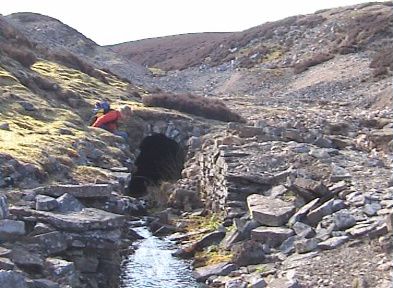 An arched stone tunnel entrance, with water flowing out.