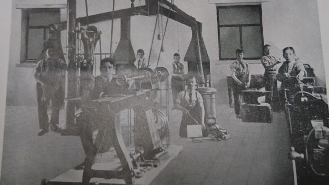 Black and white photo showing buys sat at various machines and equipment.