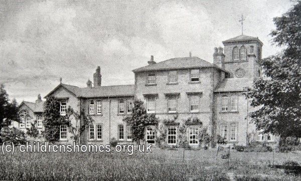 Black and white photo of a large, grand looking  building with a field at the front and several trees.