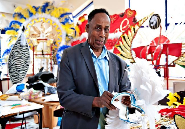 Arthur France MBE surrounded by carnival paraphanalia such as headresses and other parts of costumes.