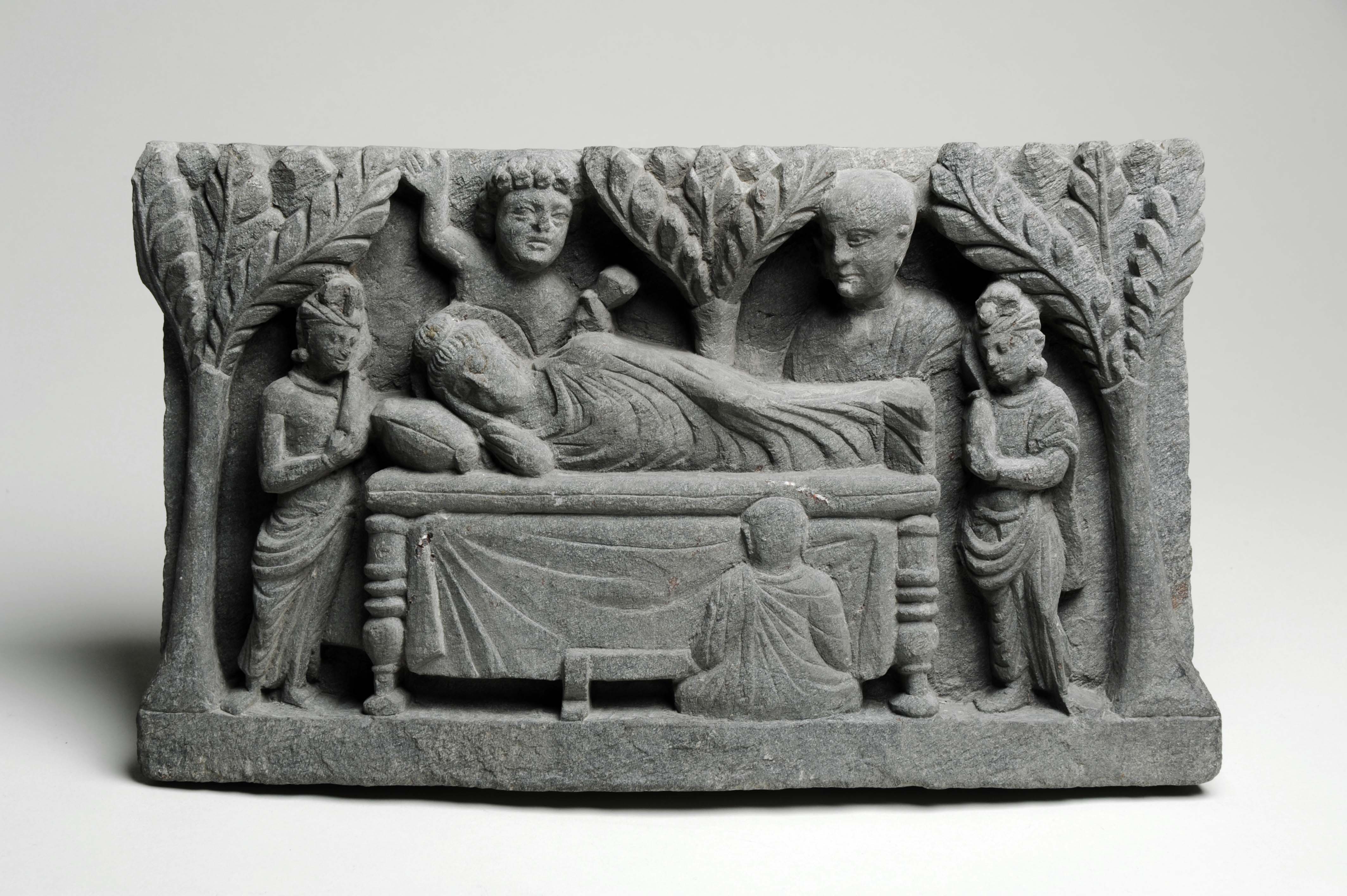 Stone carving showing the Buddha reclining on a bed, surrounded by grieving disciples.