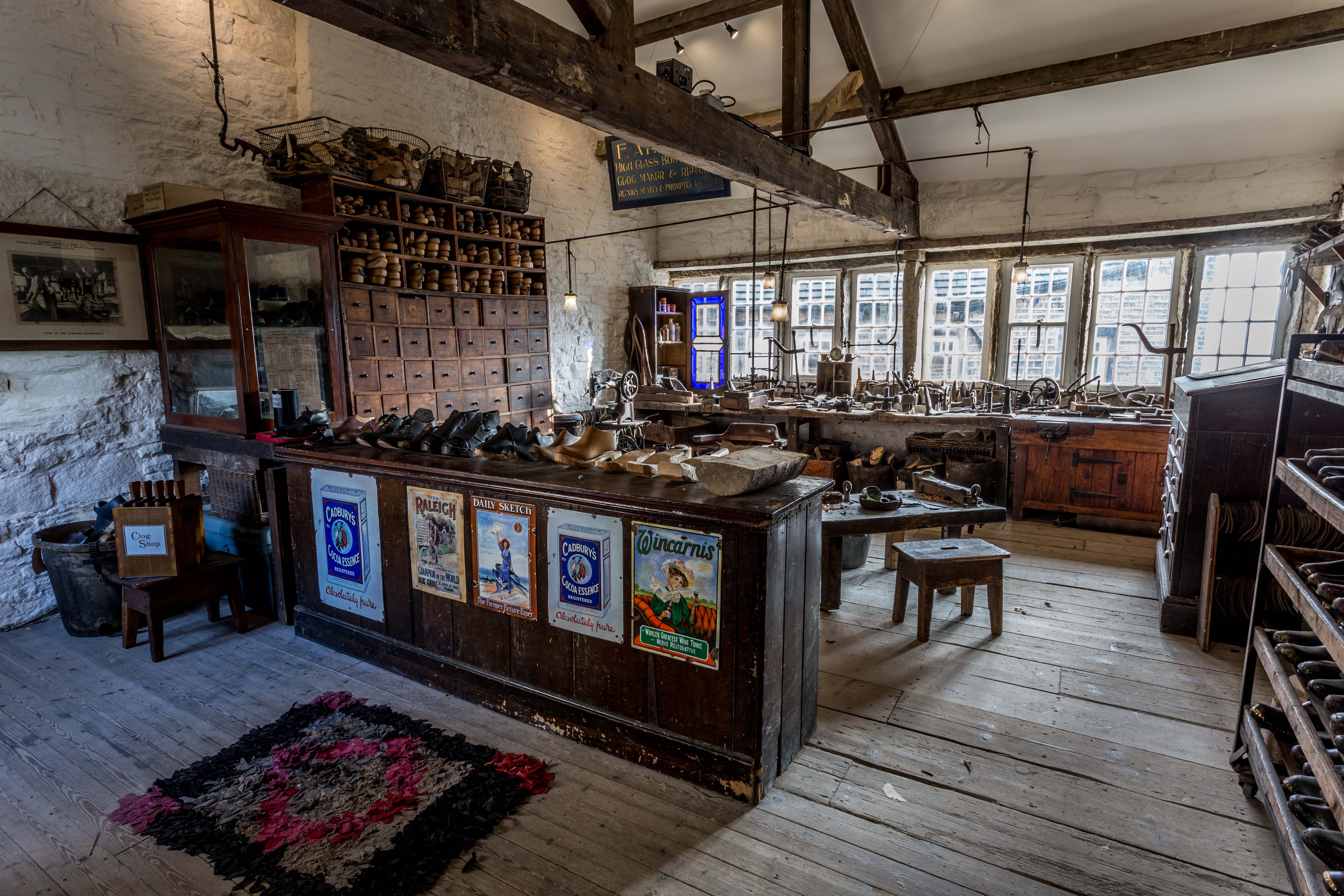 Colour photograph showing an Edwardian clog workshop with a sales counter at the front and the tools and workstations laid out behind.