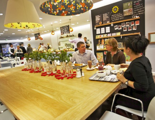 Colour photograph showing people sitting at a table with food and drink