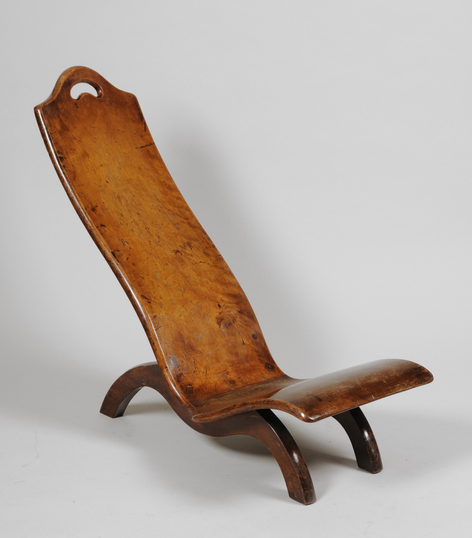 Colour photograph of a chair made from two pieces of wood. It is reclined and has only three legs - two at the front and one at the back