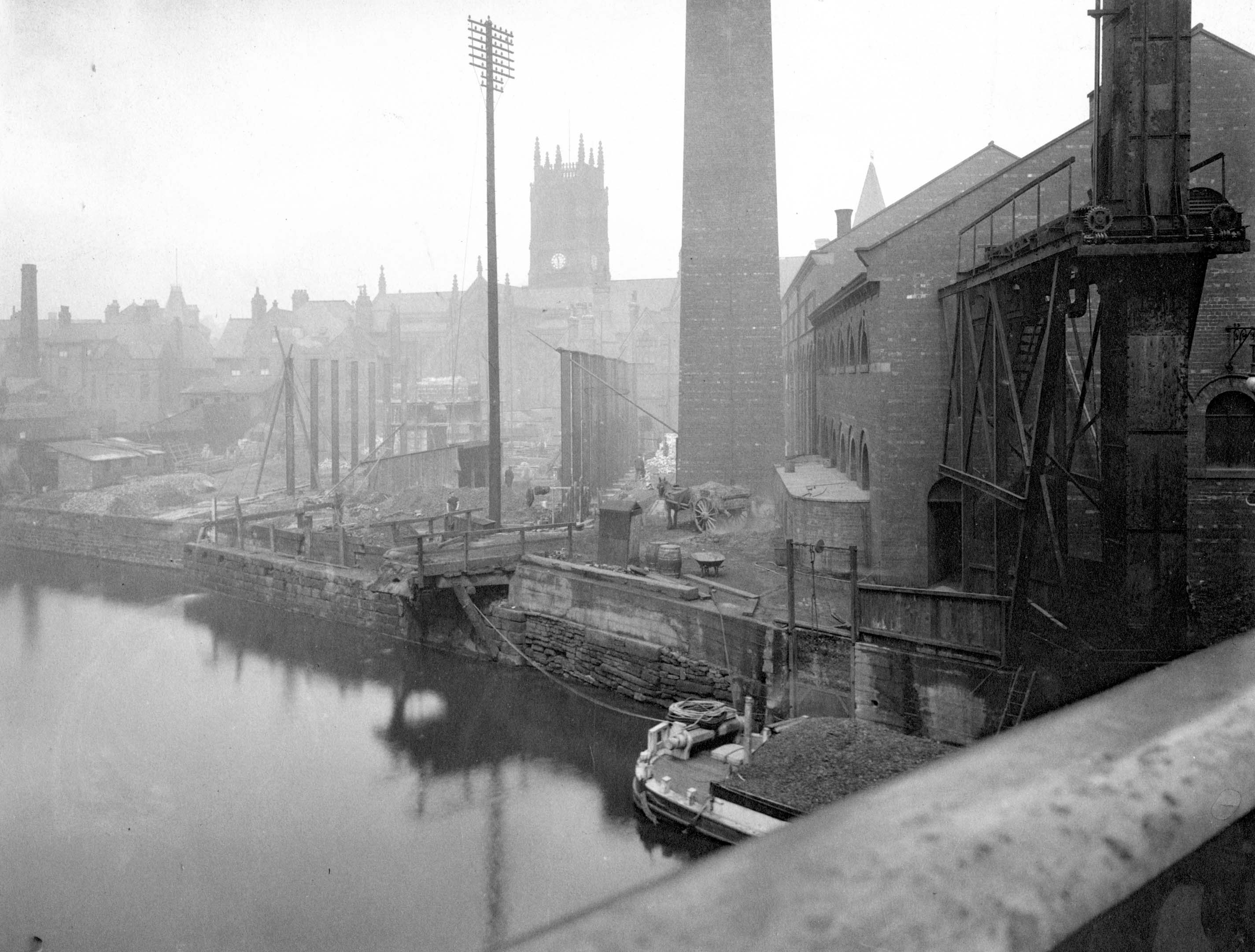 Black and white photo taken from a bridge, looking towards the Calls area, showing many buildings and a barge on the river
