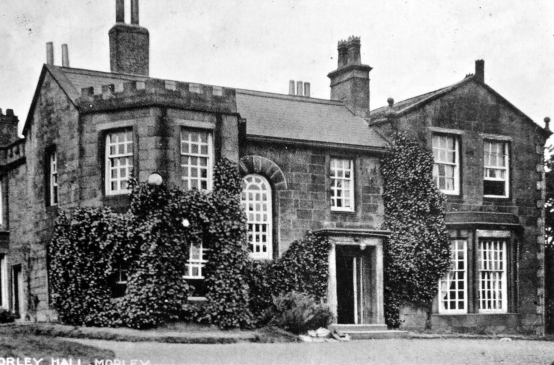 Black and white drawing of a large grand house, women in Victorian dress standing outside the railings
