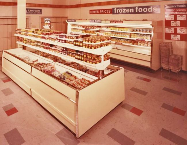 A freezer unit inside a supermarket with convenience food in tins and packets next to it
