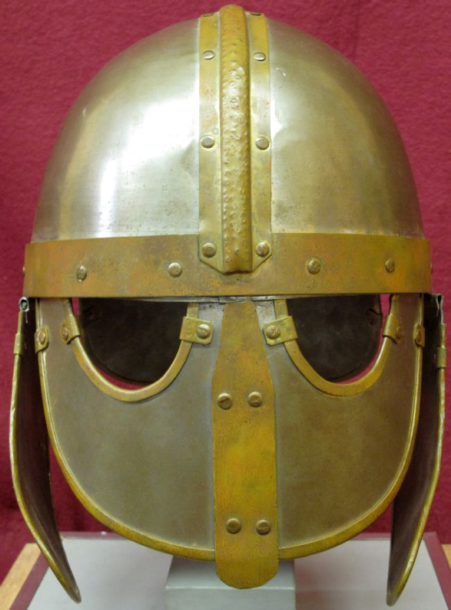 Helmet is made from a silver metal with gold coloured strips over the middle of the skull and across over the eyes.  The top half of the face is covered with metal and holes are cut for the eyes.  Metal flaps at the side protect the ears and side of the head