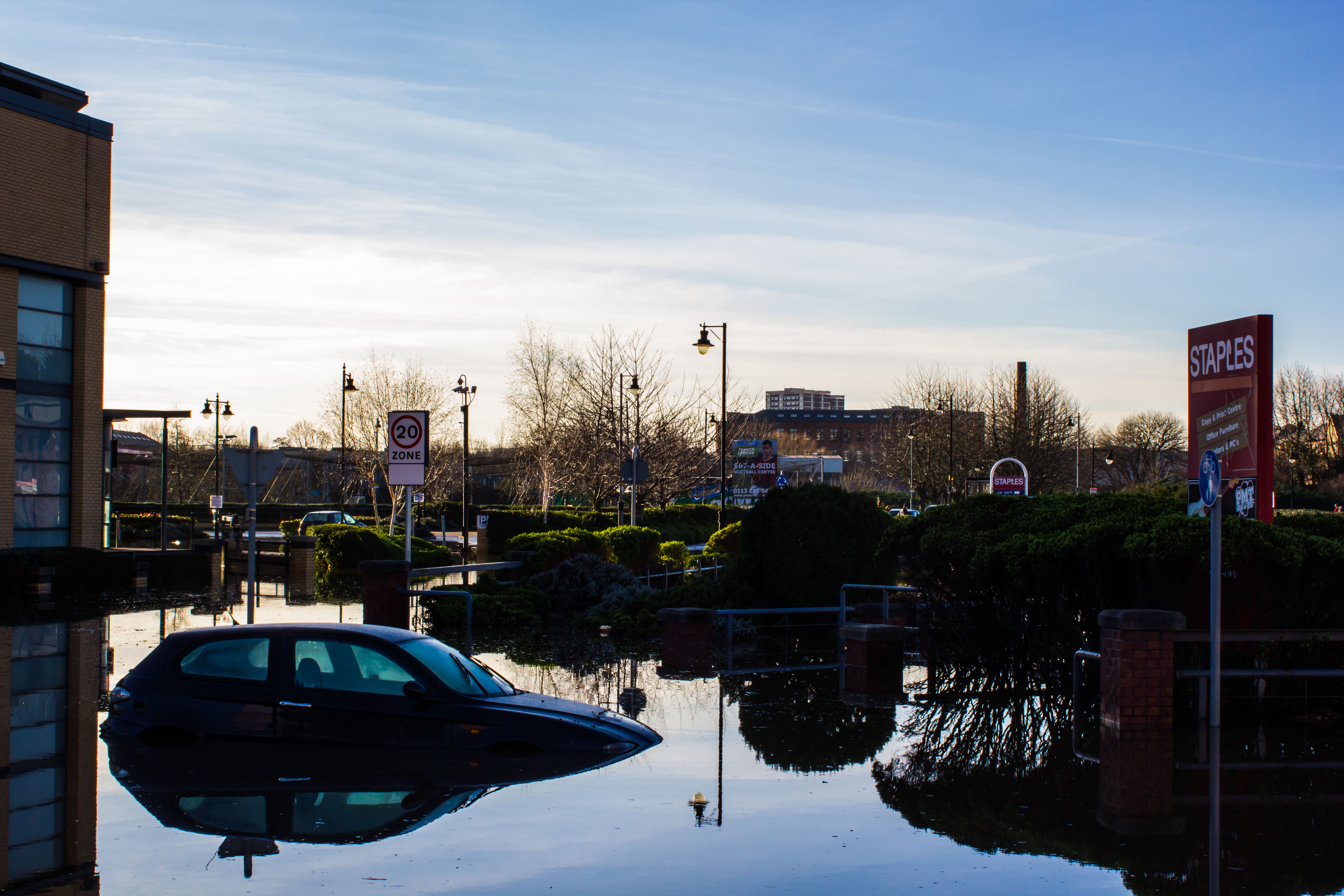 Photograph showing  a half submerged car in a shoppers car park.  The water has come over the top of the car bonnet.