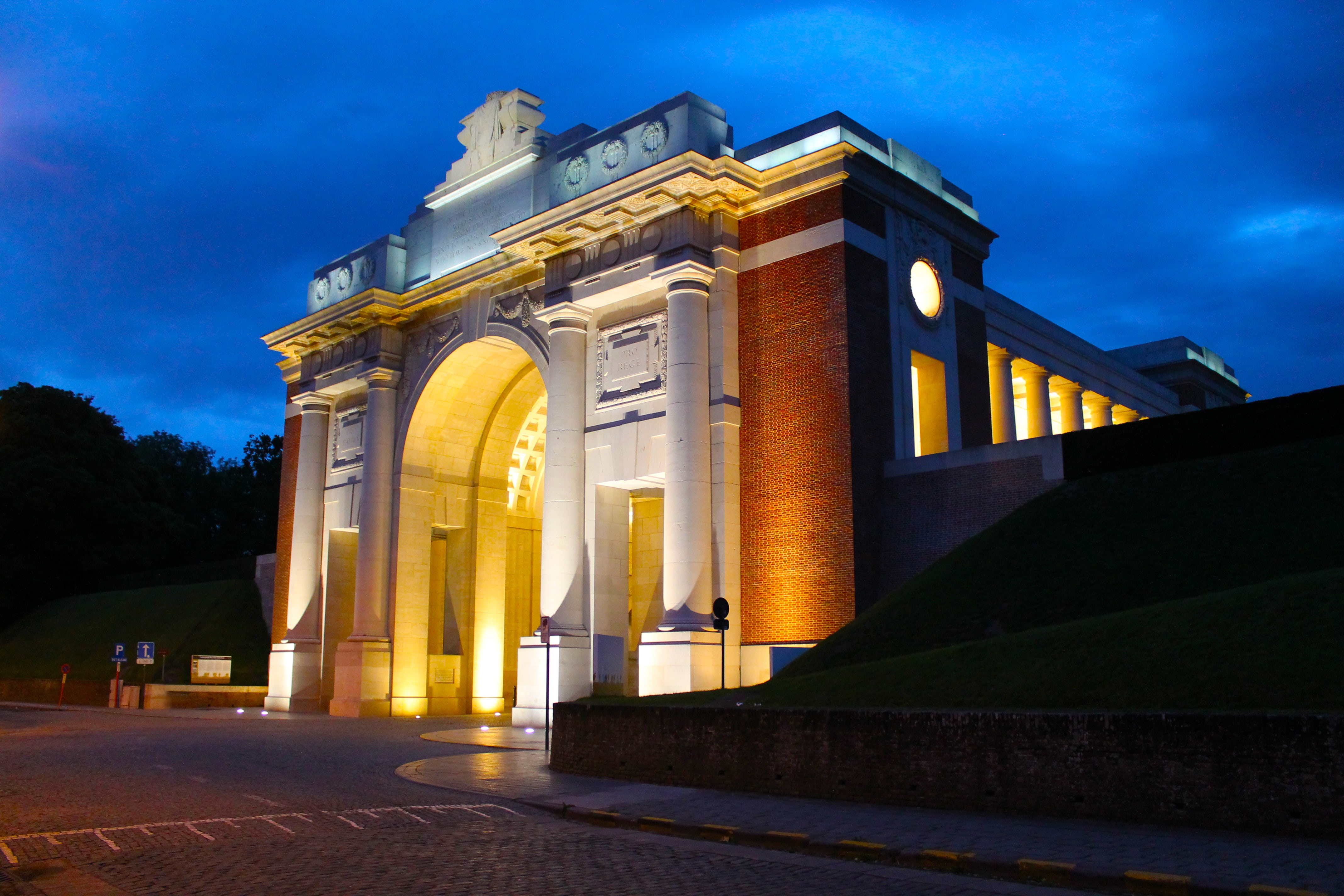 Coloured photograph showing the memorial at night. It is a big square shaped building with a huge archway running through and two columns on each side of the arch