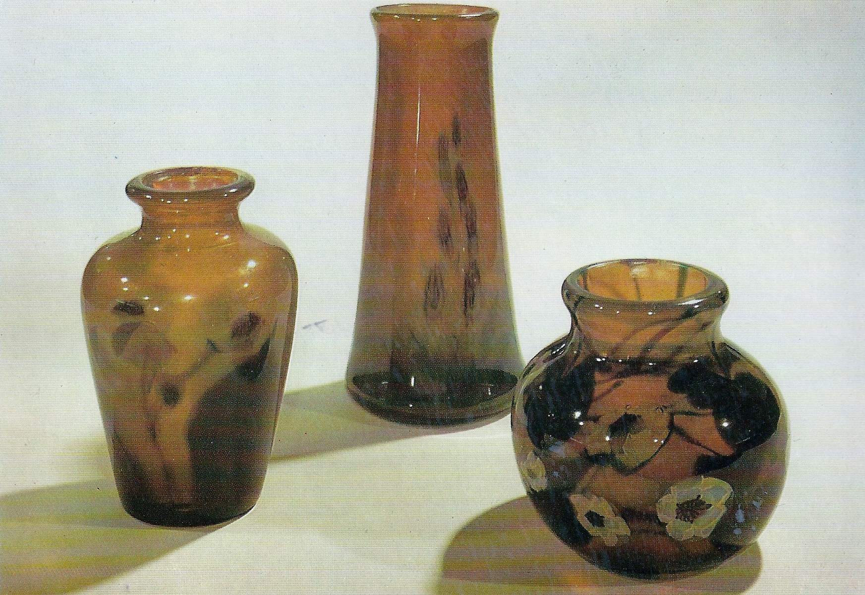 Colour photograph showing three vases of different shapes. They are all browny -green in colour, with flowers on.